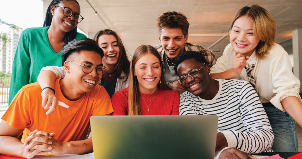 Young adults gathered around a laptop.