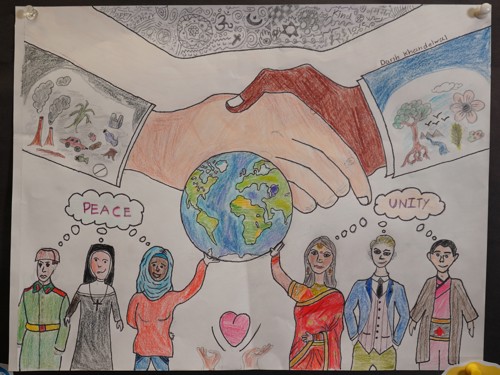 A pattern of various religious and cultural symbols along with the words "Happy together", "kind", and "love". A white hand and a black hand are holding each other. The white hand's sleeve has industrial imagery, while the black hand's sleeve has imagery of nature. In front of the shaking hands is the earth, with 6 people of different cultural and ethnic backgrounds hold it above their heads, thinking of the words "Peace" and "Unity", in the middle of the people is a pair of hands holding a heart.